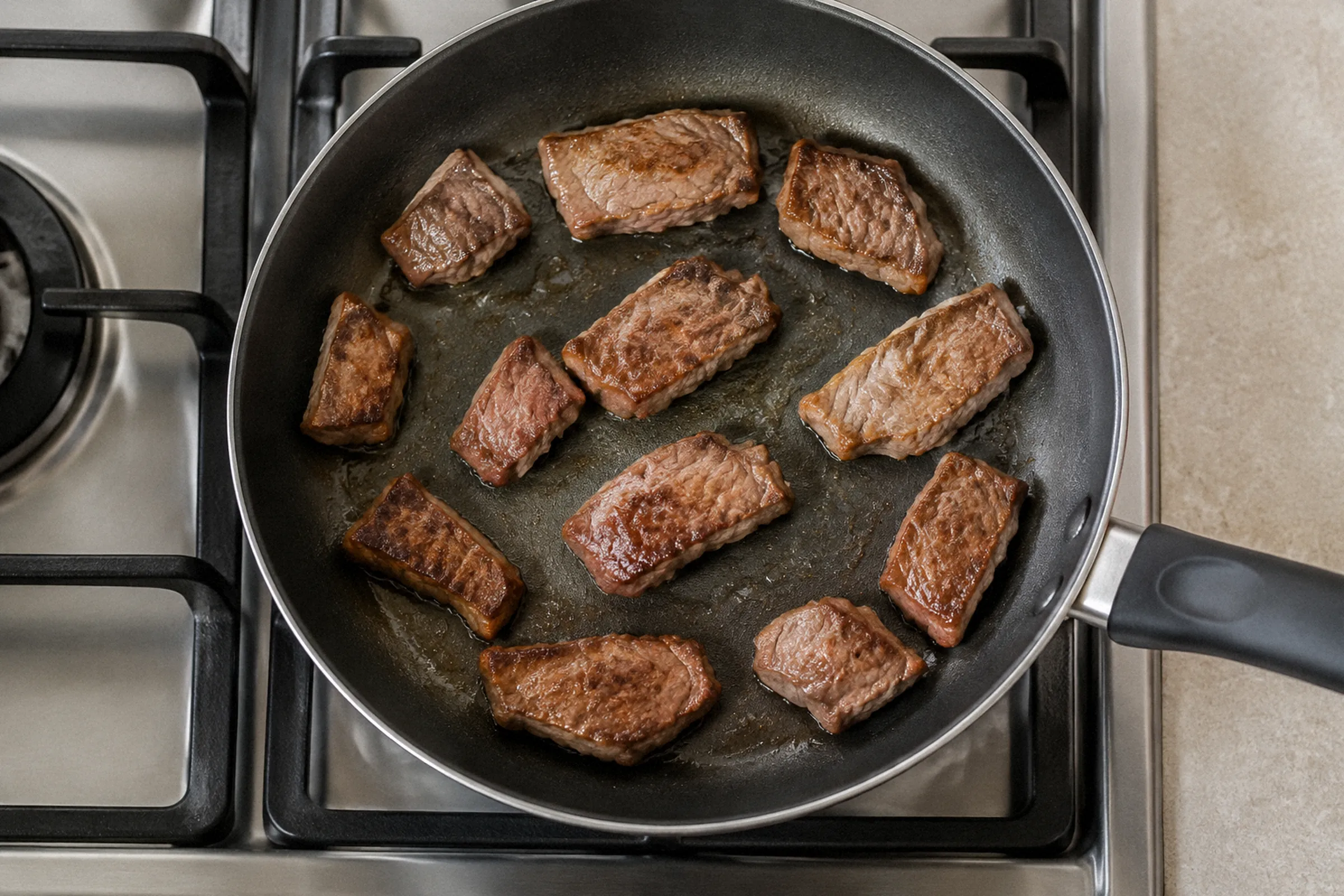 Vista superior de pedaços de carne distribuídos entre o centro e as bordas de uma frigideira sobre o fogão.